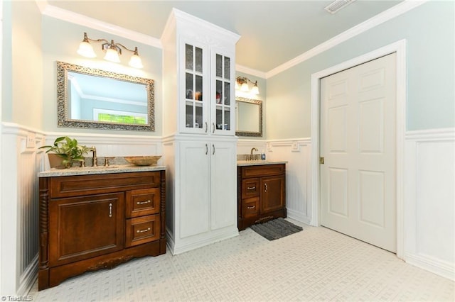 bathroom with a decorative wall, wainscoting, two vanities, and ornamental molding