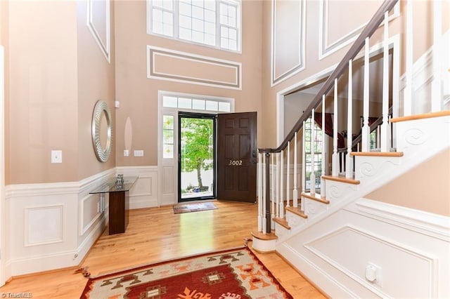 foyer featuring healthy amount of natural light, wood finished floors, stairway, a decorative wall, and a wainscoted wall