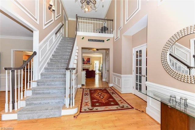 entryway featuring a chandelier, wood finished floors, stairway, ornamental molding, and a wainscoted wall