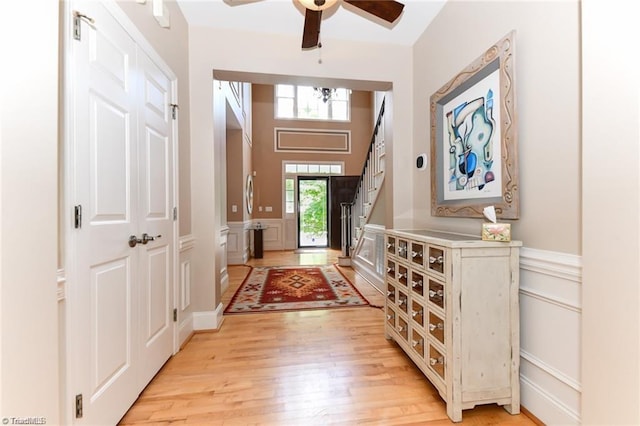 entrance foyer featuring a decorative wall, light wood-style floors, wainscoting, stairway, and a ceiling fan