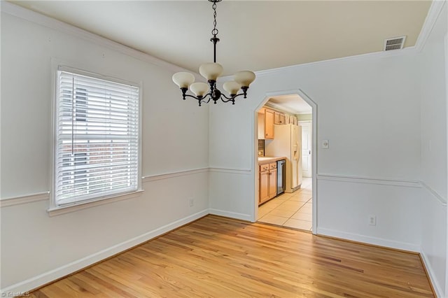 unfurnished dining area featuring ornamental molding, an inviting chandelier, and light hardwood / wood-style floors