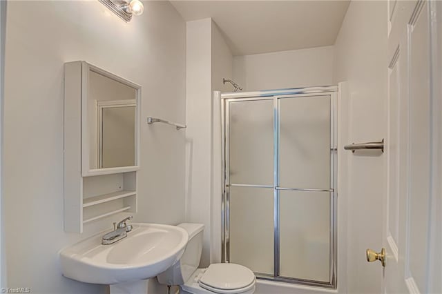 bathroom featuring toilet, a shower with door, and sink