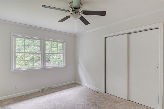 unfurnished bedroom featuring crown molding, light colored carpet, ceiling fan, and a closet