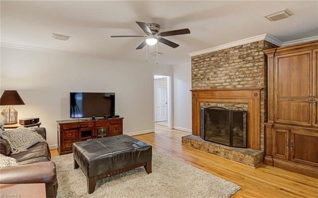 living room with light wood-type flooring, ceiling fan, a fireplace, and crown molding