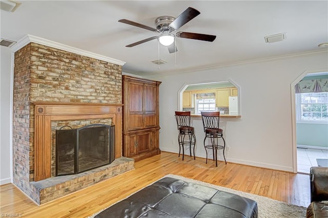 living room with a fireplace, ornamental molding, ceiling fan, and light hardwood / wood-style floors