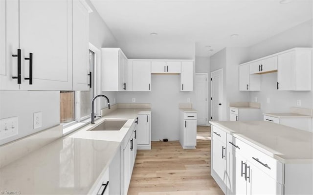 kitchen with light wood-type flooring, white cabinetry, and sink