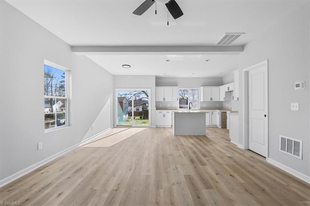 unfurnished living room with a wealth of natural light, sink, beamed ceiling, and light wood-type flooring