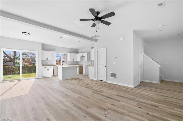 unfurnished living room with ceiling fan, beam ceiling, sink, and light hardwood / wood-style flooring