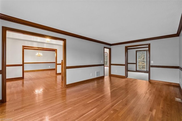 unfurnished room featuring light wood-style floors, visible vents, ornamental molding, and an inviting chandelier