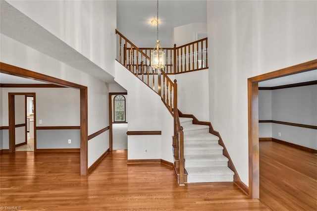 stairway featuring a towering ceiling, baseboards, and wood finished floors