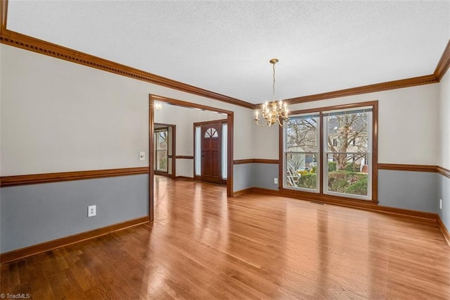 empty room featuring light wood finished floors, visible vents, an inviting chandelier, ornamental molding, and baseboards