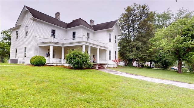 view of front facade featuring a balcony, a porch, a chimney, central AC, and a front yard