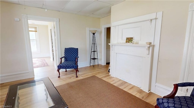 living area featuring light wood-style flooring, baseboards, and a drop ceiling