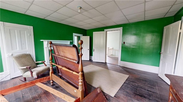bedroom with a drop ceiling, baseboards, and hardwood / wood-style flooring
