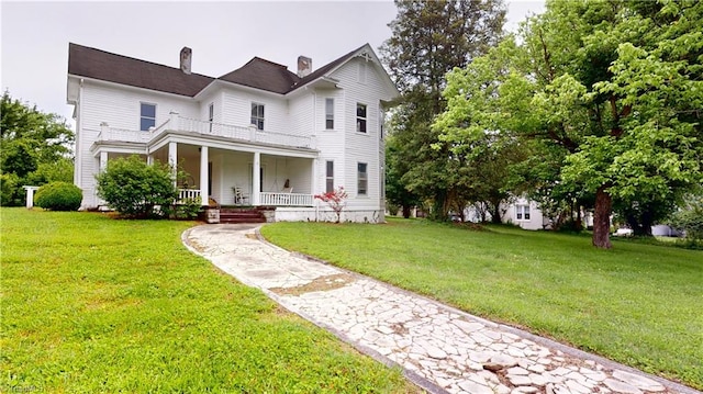 view of front of property with a porch, a balcony, a front yard, a chimney, and driveway