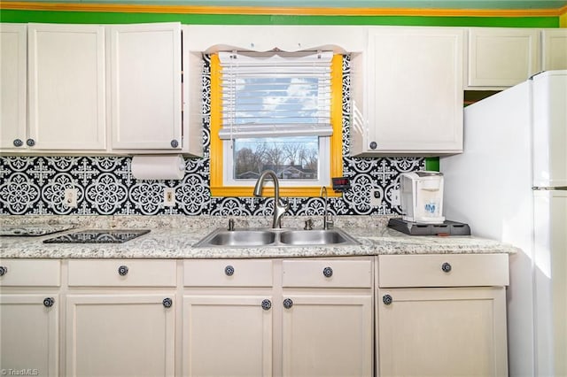 kitchen featuring sink, white refrigerator, white cabinets, and light stone counters