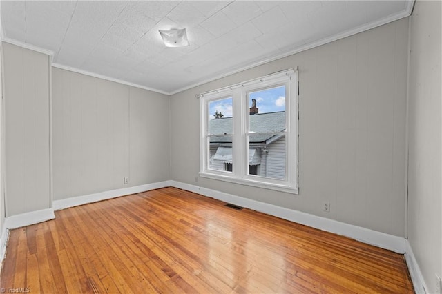 spare room with ornamental molding, wood-type flooring, visible vents, and baseboards