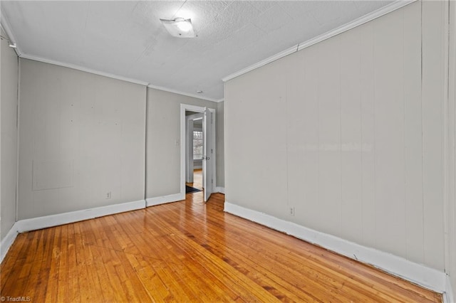 spare room featuring light wood-style floors, baseboards, and crown molding