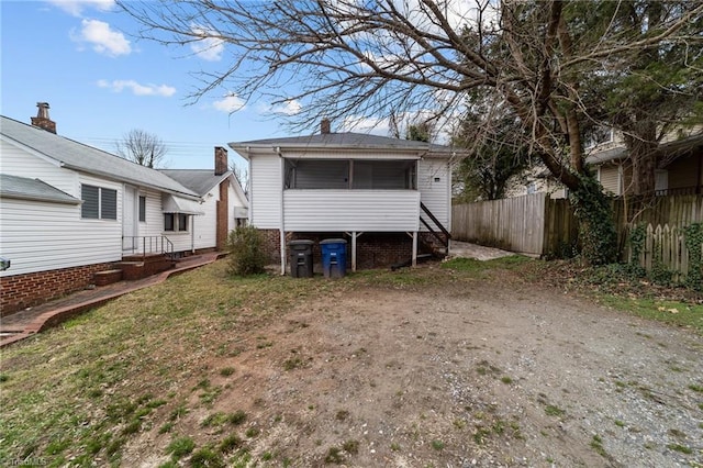 back of property with dirt driveway, fence, and a sunroom