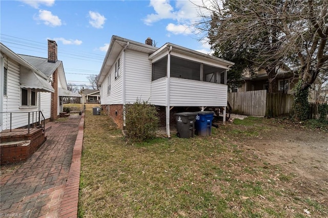 view of property exterior featuring a lawn, a sunroom, a chimney, fence, and central AC