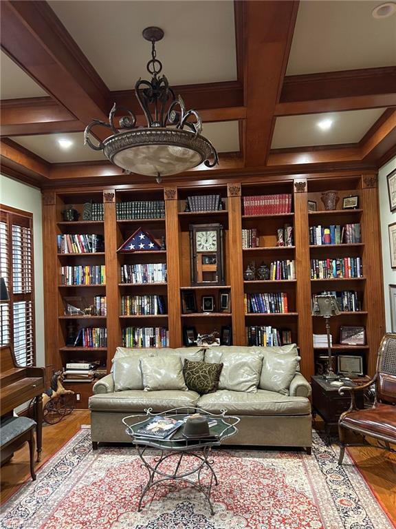 living room featuring hardwood / wood-style floors, a chandelier, beamed ceiling, built in features, and coffered ceiling