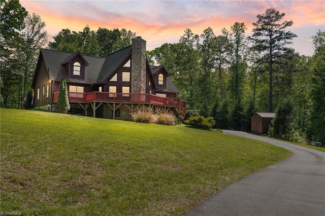 back of house with a lawn, a chimney, an outdoor structure, and a storage unit