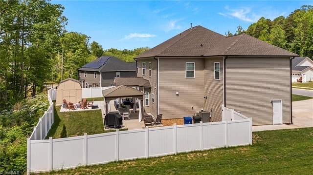 back of house with a lawn, a patio, a fenced backyard, a shingled roof, and a gazebo