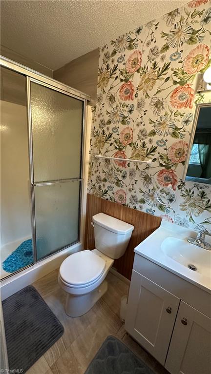 bathroom featuring vanity, toilet, a textured ceiling, and an enclosed shower