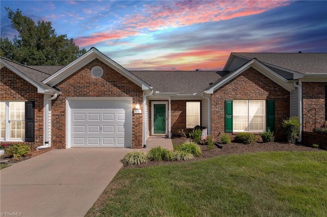 ranch-style home with concrete driveway, roof with shingles, an attached garage, a yard, and brick siding