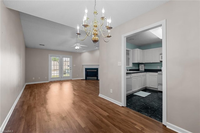 unfurnished living room with ceiling fan with notable chandelier, baseboards, dark wood-style flooring, and a glass covered fireplace