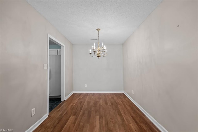 unfurnished dining area with a textured ceiling, baseboards, dark wood finished floors, and a notable chandelier