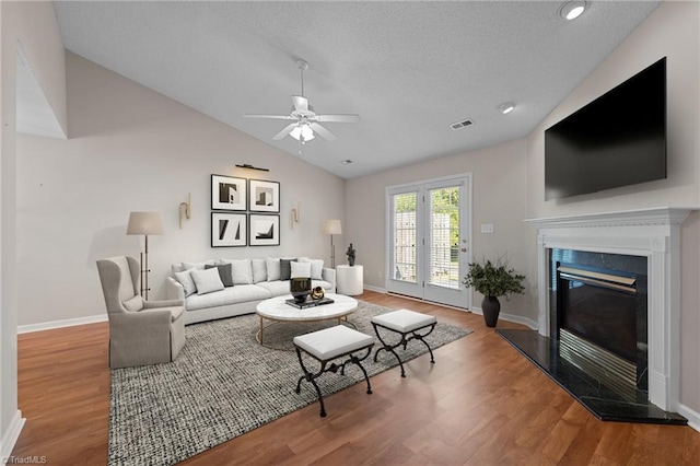 living area featuring lofted ceiling, visible vents, a glass covered fireplace, wood finished floors, and baseboards