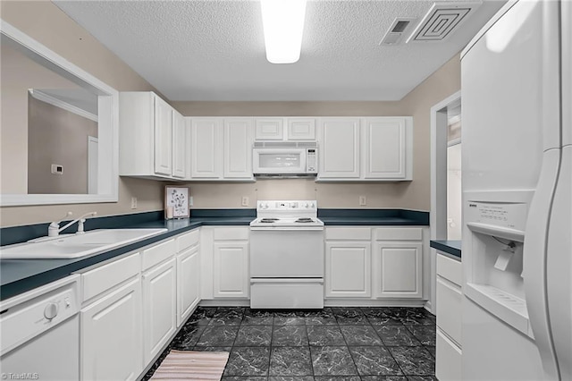 kitchen featuring white appliances, visible vents, dark countertops, white cabinetry, and a sink