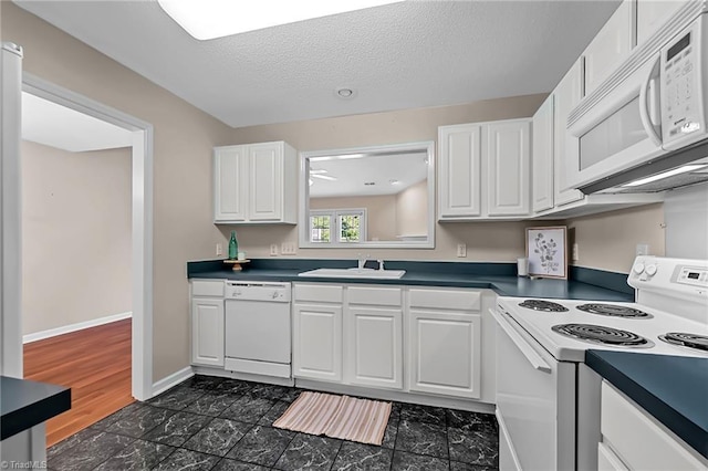 kitchen with white appliances, dark countertops, and white cabinetry