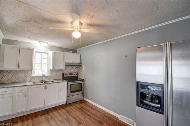 kitchen with stainless steel appliances, a sink, white cabinets, light wood-style floors, and decorative backsplash