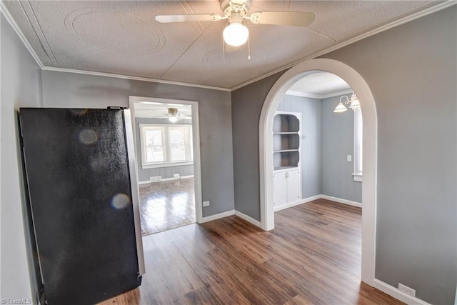 spare room with arched walkways, ceiling fan, wood finished floors, baseboards, and ornamental molding