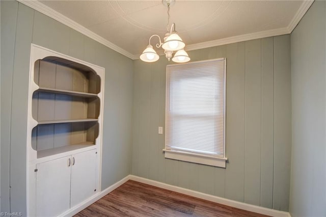 unfurnished dining area featuring a notable chandelier, baseboards, wood finished floors, and crown molding