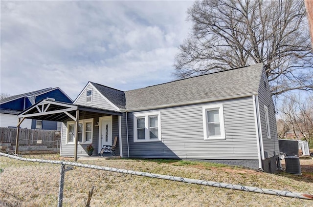 view of front of property with roof with shingles, a front yard, fence, and central air condition unit