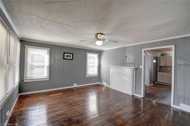 unfurnished living room with visible vents, baseboards, a ceiling fan, wood-type flooring, and crown molding