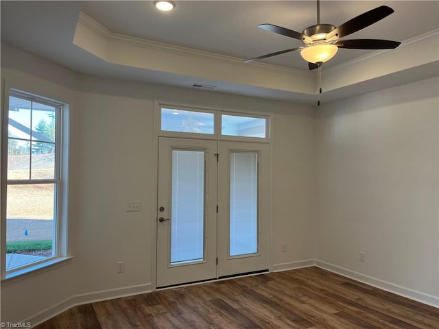 doorway to outside with baseboards, a tray ceiling, dark wood finished floors, and crown molding