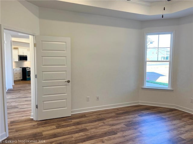 spare room featuring dark wood-type flooring, crown molding, and baseboards