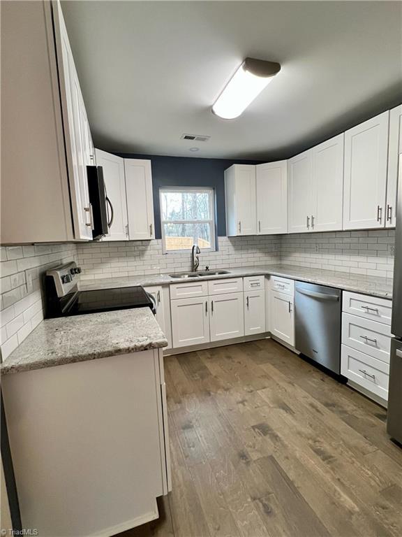 kitchen with light stone countertops, stainless steel appliances, sink, hardwood / wood-style flooring, and white cabinetry