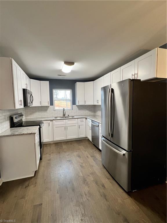 kitchen featuring sink, dark hardwood / wood-style floors, tasteful backsplash, white cabinetry, and stainless steel appliances