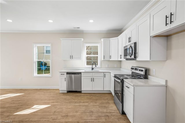 kitchen featuring appliances with stainless steel finishes, ornamental molding, light countertops, white cabinetry, and a sink