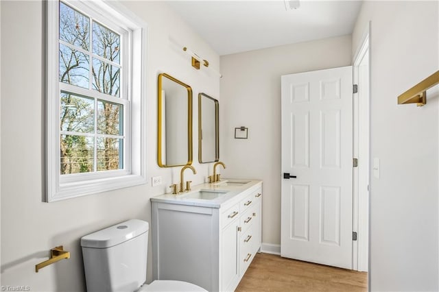 bathroom featuring double vanity, toilet, a sink, and wood finished floors