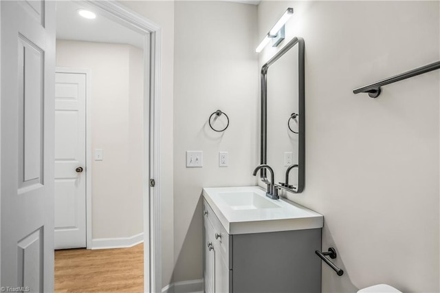 half bathroom featuring baseboards, wood finished floors, and vanity