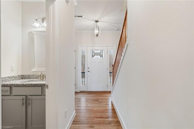 corridor featuring baseboards, visible vents, light wood-style flooring, a sink, and stairs