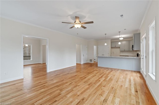 unfurnished living room featuring visible vents, baseboards, ornamental molding, light wood-style flooring, and a ceiling fan