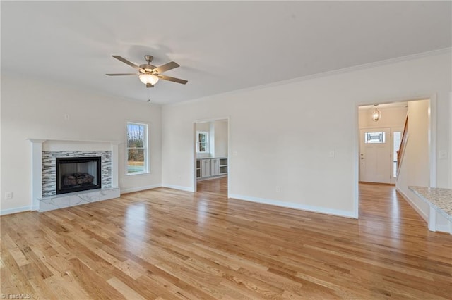 unfurnished living room featuring light wood-style flooring, a tiled fireplace, ornamental molding, baseboards, and ceiling fan