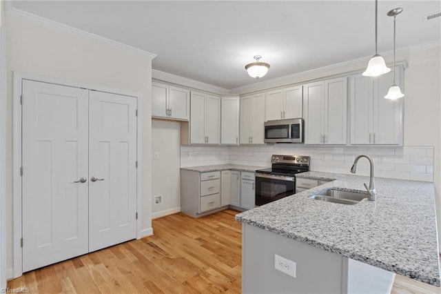 kitchen with light stone counters, a peninsula, a sink, ornamental molding, and stainless steel appliances